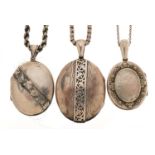 Three Victorian white metal lockets on necklaces including two silver, the largest 5.8cm high, total