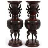 Pair of Japanese patinated bronze three footed vases with twin handles on circular bases, each