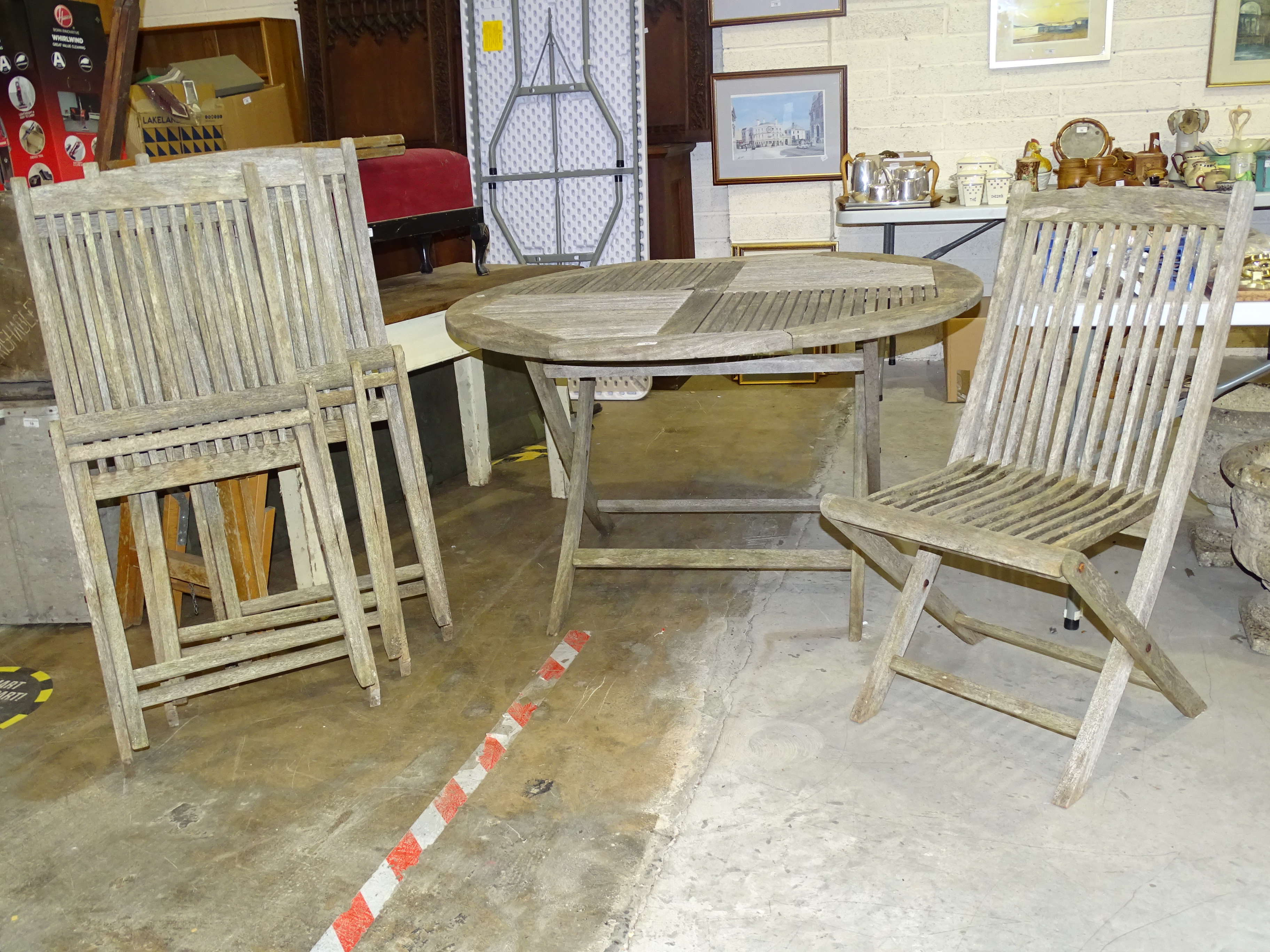 A weathered teak circular slatted-top patio table, 125cm diameter and four matching folding chairs.