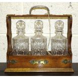 An oak and brass-mounted Tantalus, 34cm wide, 34cm high, with three glass decanters and stoppers.