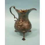 A George III silver baluster cream jug with embossed foliate and scroll decoration and leaf-capped