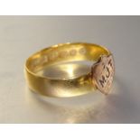 A gold wedding band with small initialled shield attached, (marks obliterated), size M, 3g.