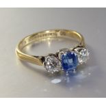 A sapphire and diamond ring, claw-set a step-cut sapphire between two brilliant-cut diamonds,