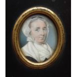 An early 19th century oval portrait miniature of a mature lady wearing a white cap and fichu, 38 x