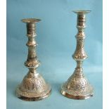 Two Asian white metal candlesticks with profusely-chased decoration, 23cm high and 20cm high, (2).