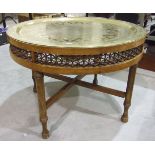 A large brass Benares circular tray, 70cm diameter, set in a low wood table with pierced frieze,