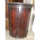 A George III mahogany bow-fronted hanging corner cupboard with dentil cornice, 74cm wide, 114cm
