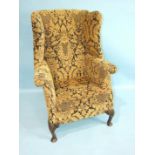 A Georgian upholstered wing armchair on short cabriole shell-carved front legs.