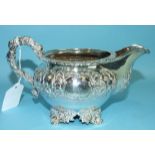 A William IV silver cream jug with embossed decoration, raised on cast foliate feet, marks rubbed,