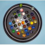 An ebony circular solitaire board, 30cm diameter, together with a collection of glass marbles.