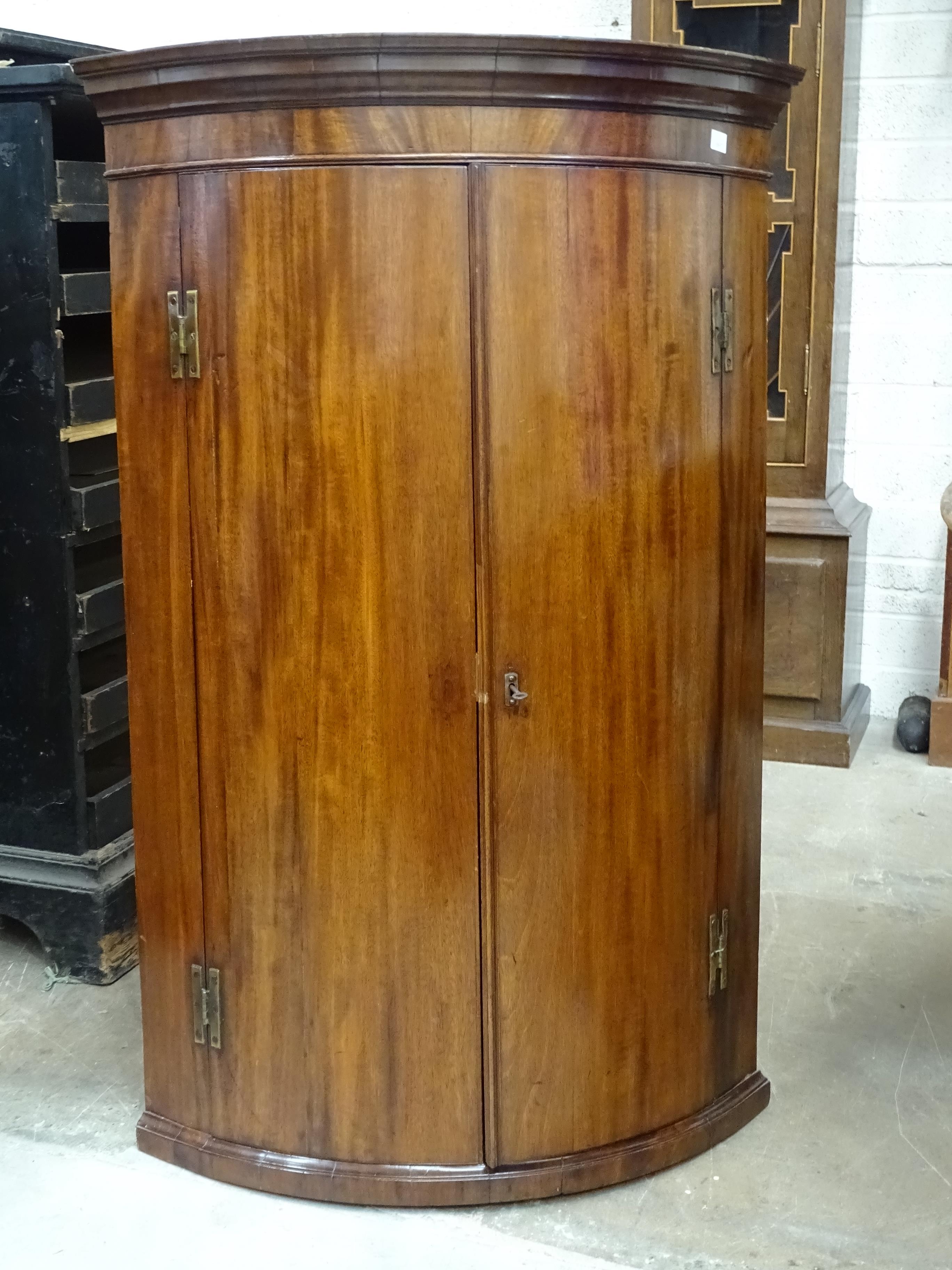 A Georgian mahogany bow fronted two-door hanging wall corner cupboard,76cm wide, 116cm high.