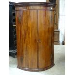 A Georgian mahogany bow fronted two-door hanging wall corner cupboard,76cm wide, 116cm high.