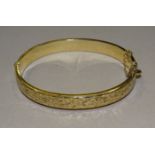 A 9ct gold hinged bangle with engraved scroll decoration, 8mm wide, 9.5g.