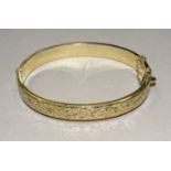 A 9ct gold hinged bangle with engraved scroll decoration, 8mm wide, 9.5g.