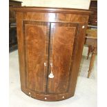A Georgian mahogany bow-fronted corner cupboard, having a pair of rosewood-banded doors above a