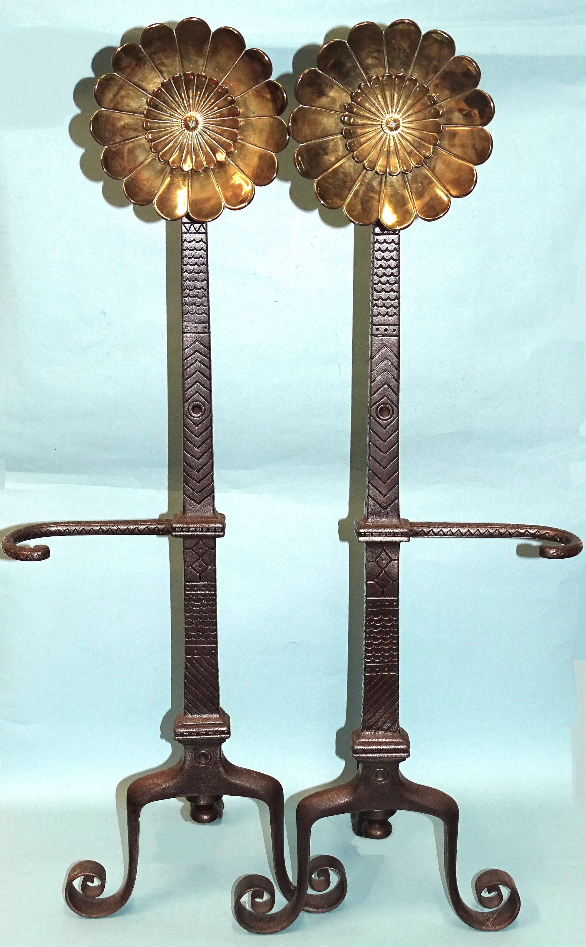 A pair of iron fire dogs in the Arts & Crafts style, each decorated overall with geometric designs