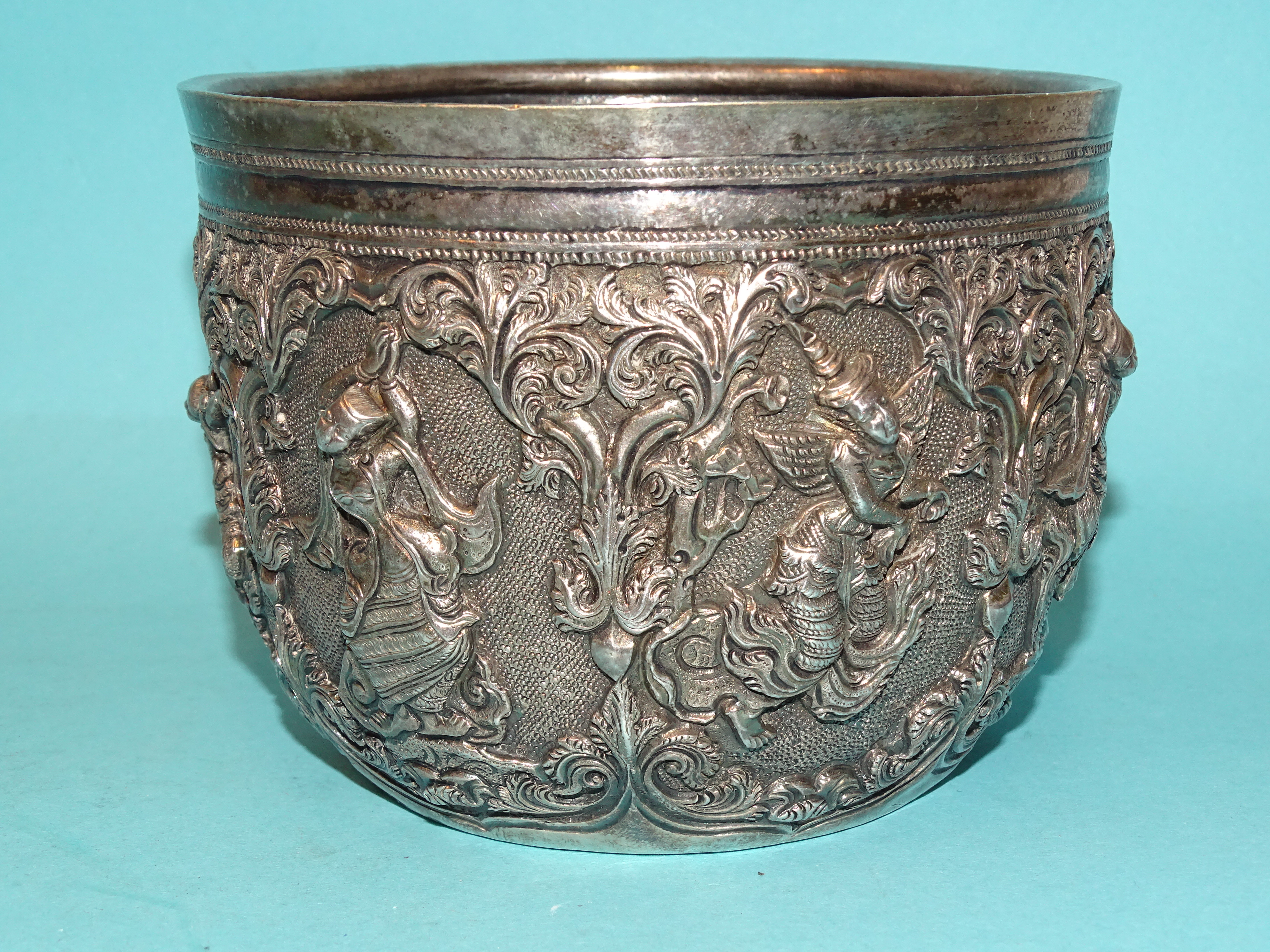 A Burmese silver bowl deeply embossed with deities within scrolling arches, 12.5cm diameter, 9.5cm