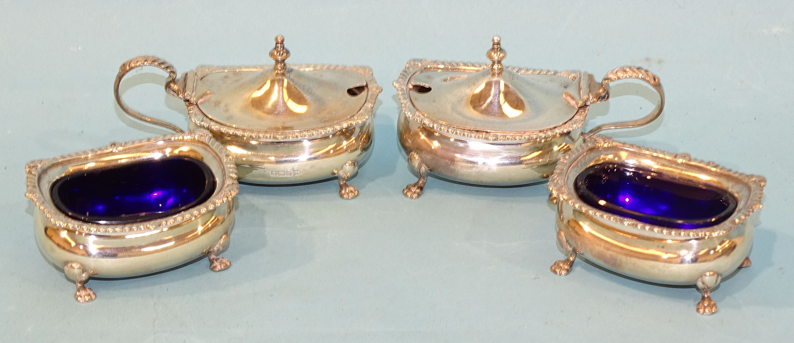 A four-piece silver cruet of oval bellied form, with cast rims, four paw feet and two blue glass