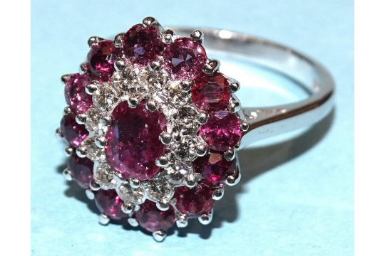 A ruby and diamond cluster ring claw-set an oval ruby within concentric borders of twelve each - Image 1 of 2