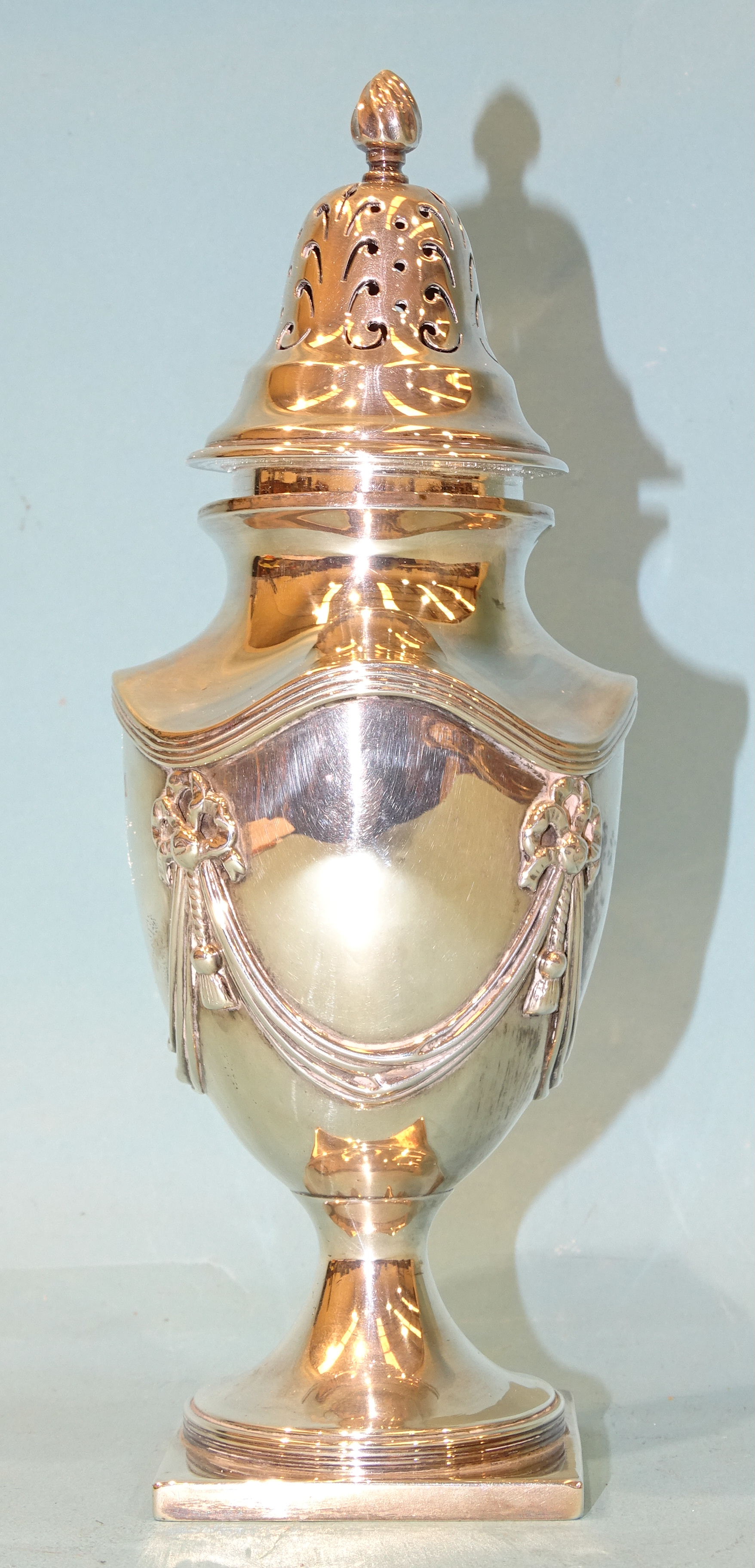 A silver sugar sifter of urn form with applied swag and tassel decoration, raised on square foot,