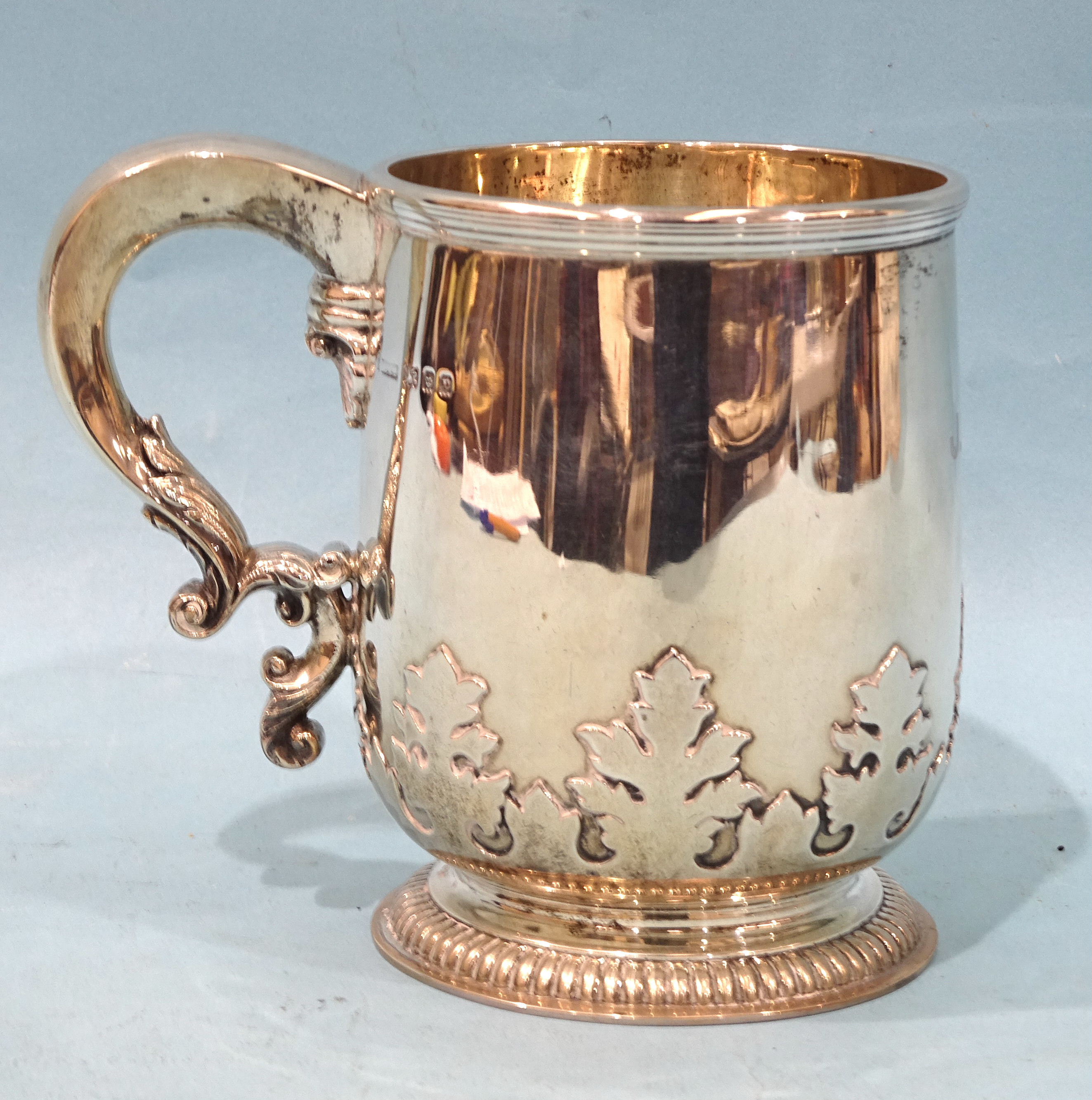 A silver tankard with applied leaf frieze and scroll handle, raised on gadrooned foot, Asprey &