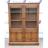 Ercol stained oak display cabinet, with twin bevelled glazed doors over panelled cupboard doors,