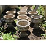 Set of seven reconstituted stone campana shape garden urns, with reeded sides and square bases,