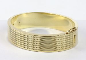 Gold hinged bangle, oval bangle with a lined pattern design, with safety clasp, in stamped 14ct