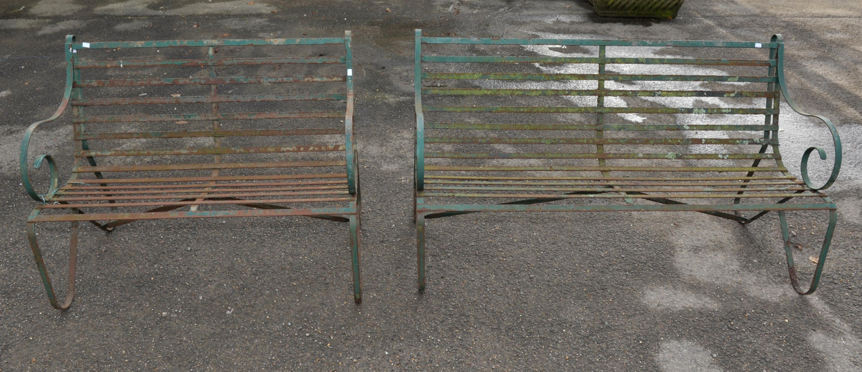 Two wrought iron green painted garden benches, scrolling arms and legs with slatted seats,