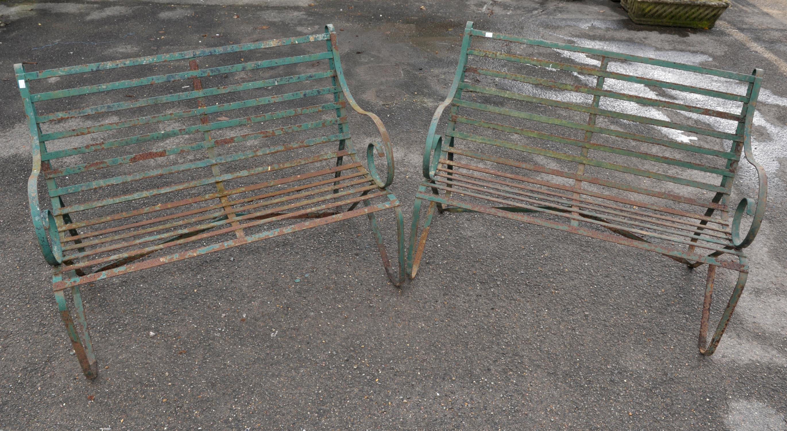 Two wrought iron green painted garden benches, scrolling arms and legs with slatted seats,