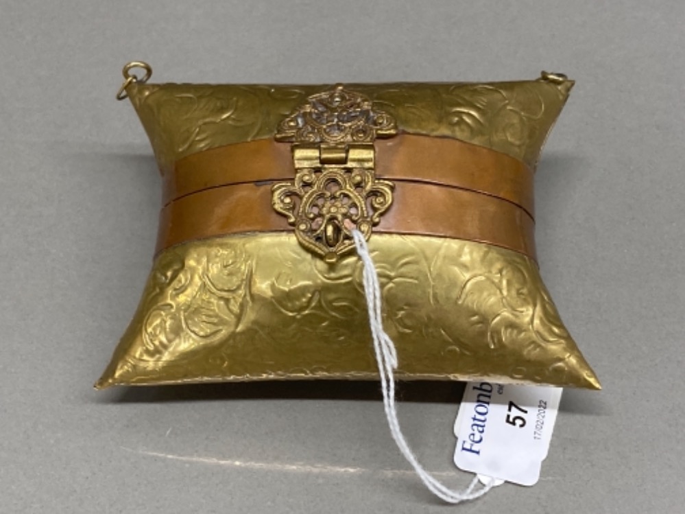 A brass purse in the form of a pillow, with intricate clasp
