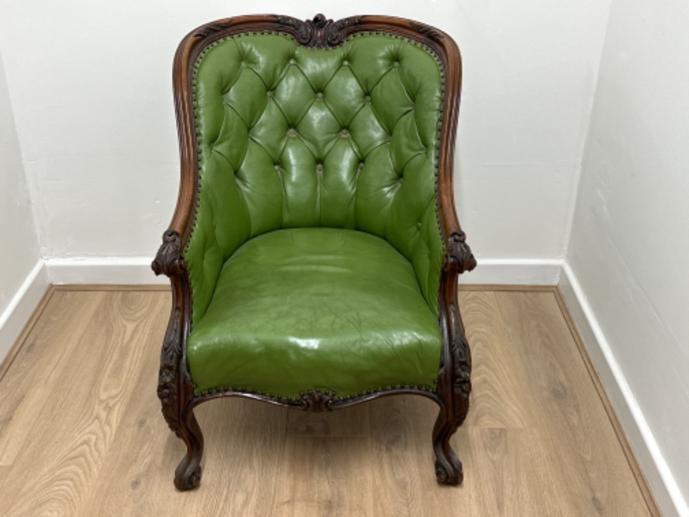 An elegant antique heavily carved mahogany framed green leather button backed gents armchair