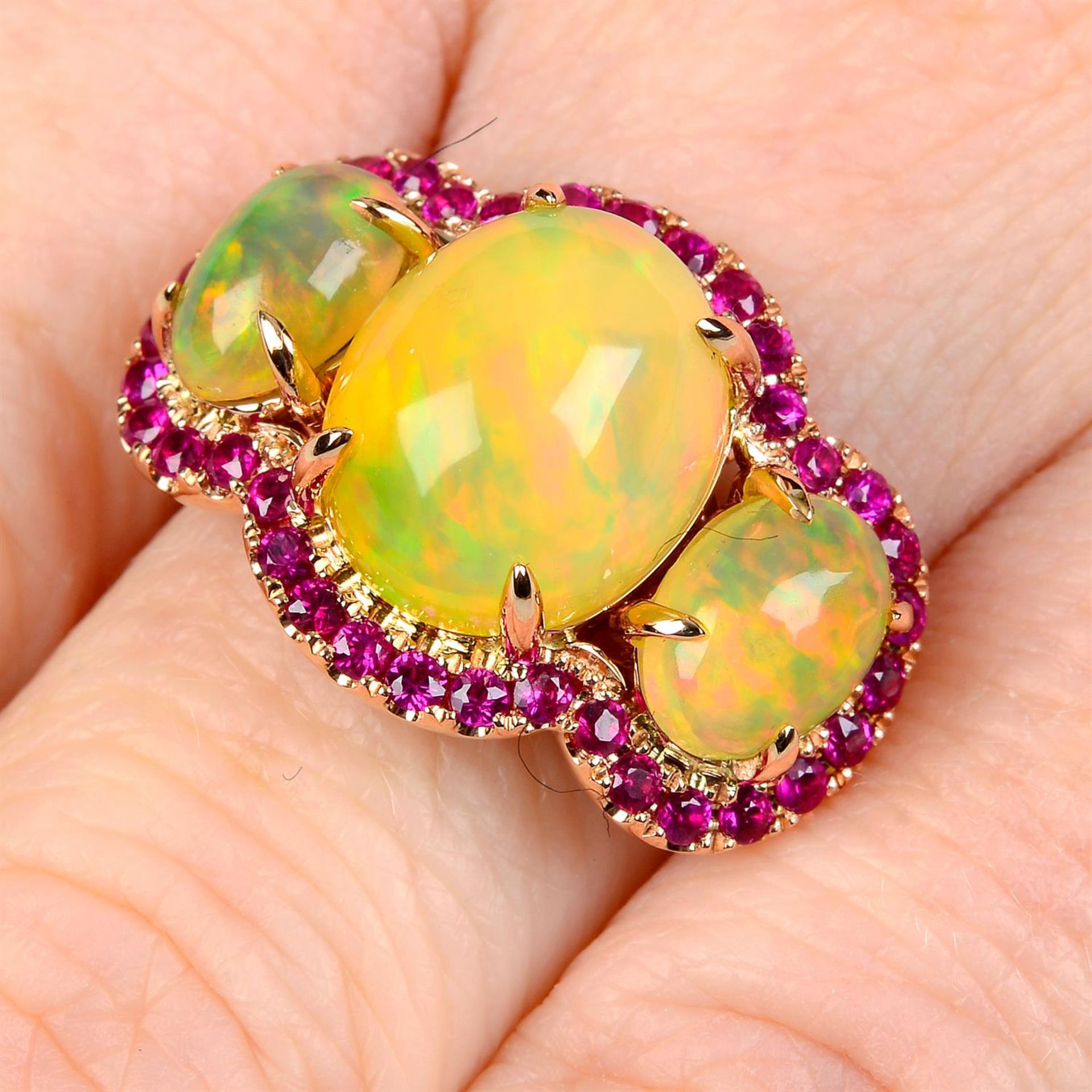 A graduated opal three-stone ring, with ruby shared surround.