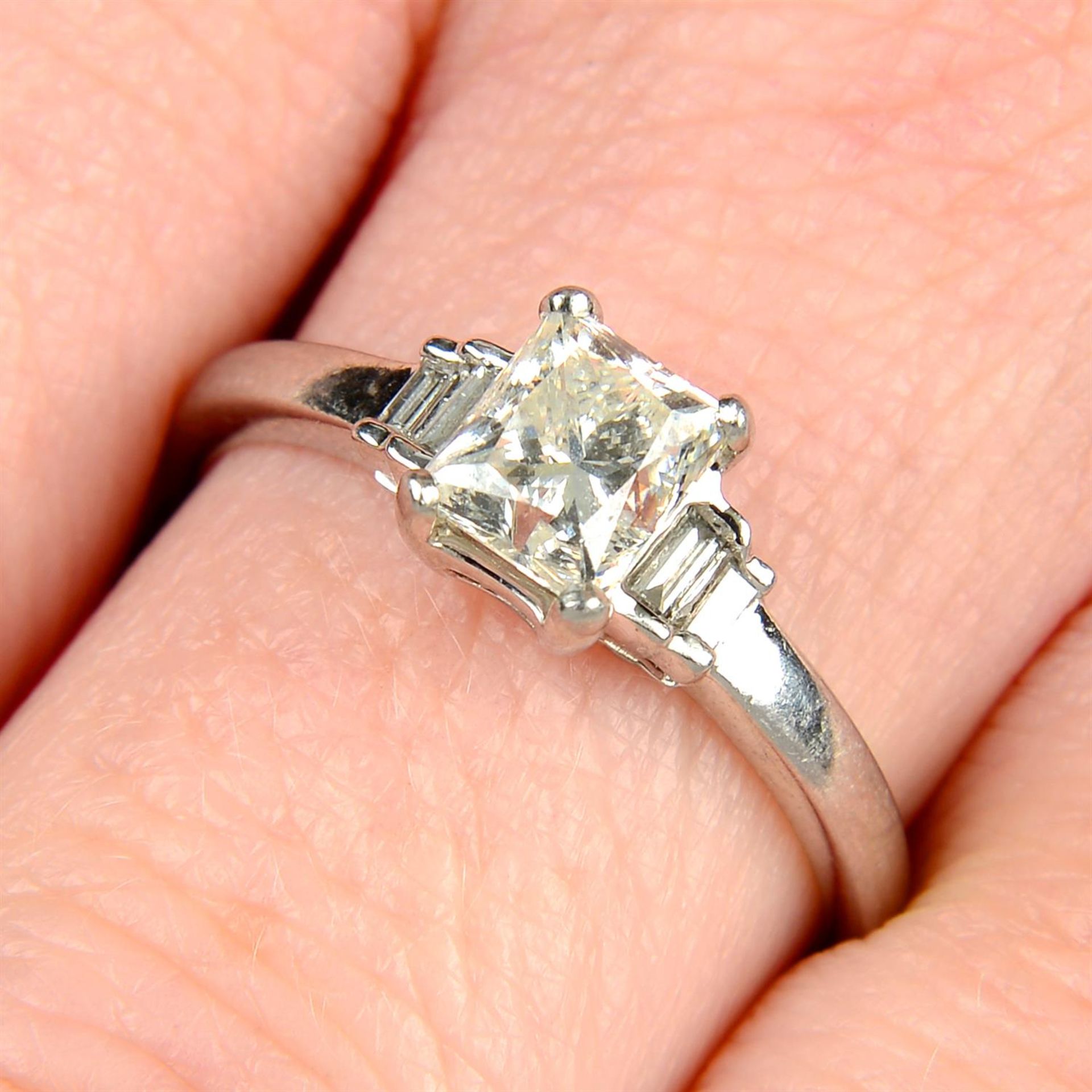 A platinum rectangular-shape diamond single-stone ring, with baguette-cut diamond shoulders.