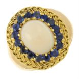 A coral cabochon and sapphire cluster ring, with woven surround and engraved shoulders.