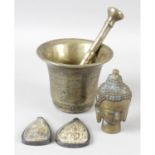 A metal study depicting the head of a Buddha, bronze pestle and mortar and two Eastern amulets. (3)