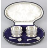 A cased pair of 1920's silver open salts, together with a pair of associated salt spoons.