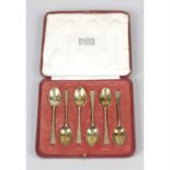 A cased set of silver-gilt coffee spoons & a cased set of silver and enamel cocktail sticks.