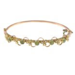 An early 20th century 9ct gold peridot and split pearl hinged bangle.