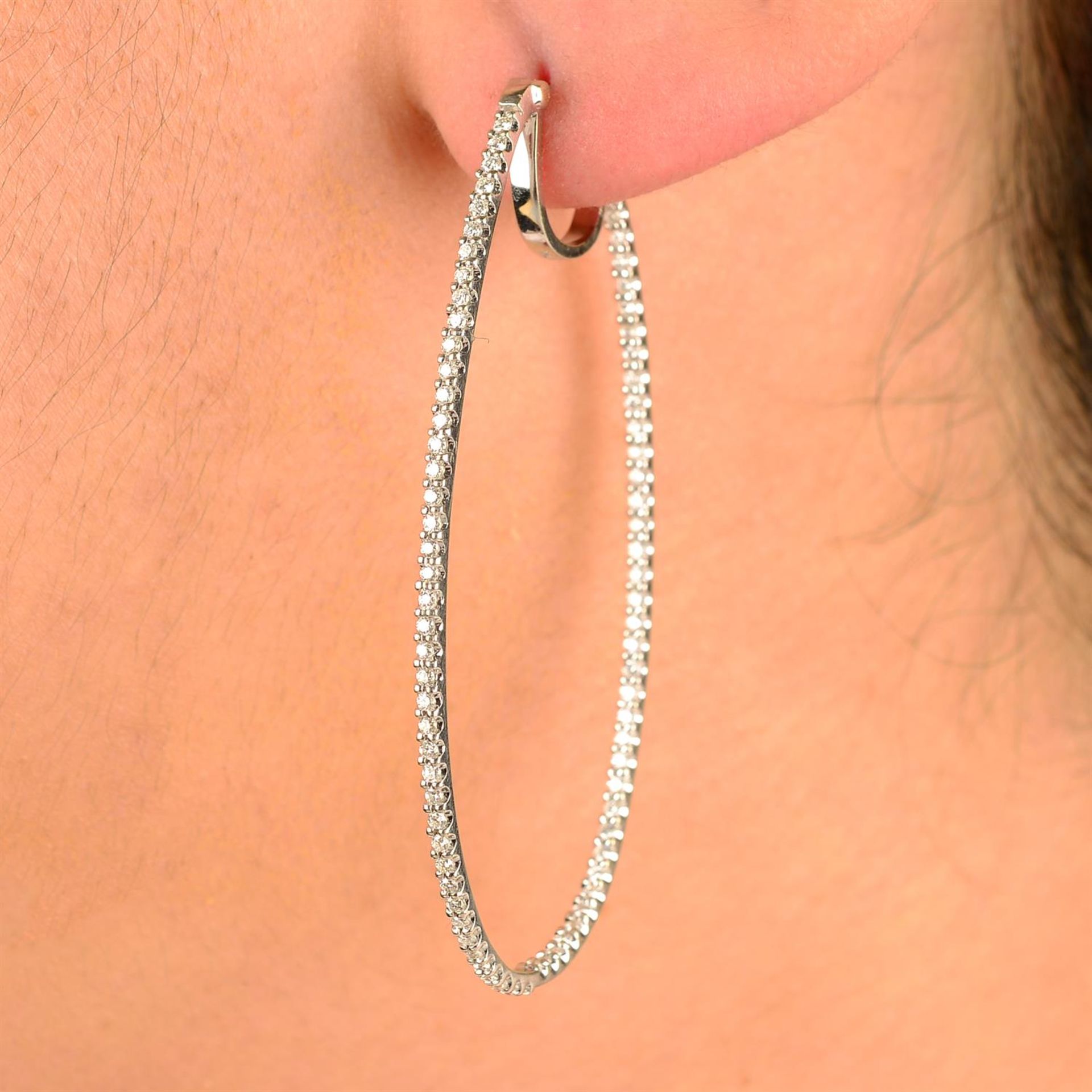 A pair of brilliant-cut diamond oval hoop earrings.