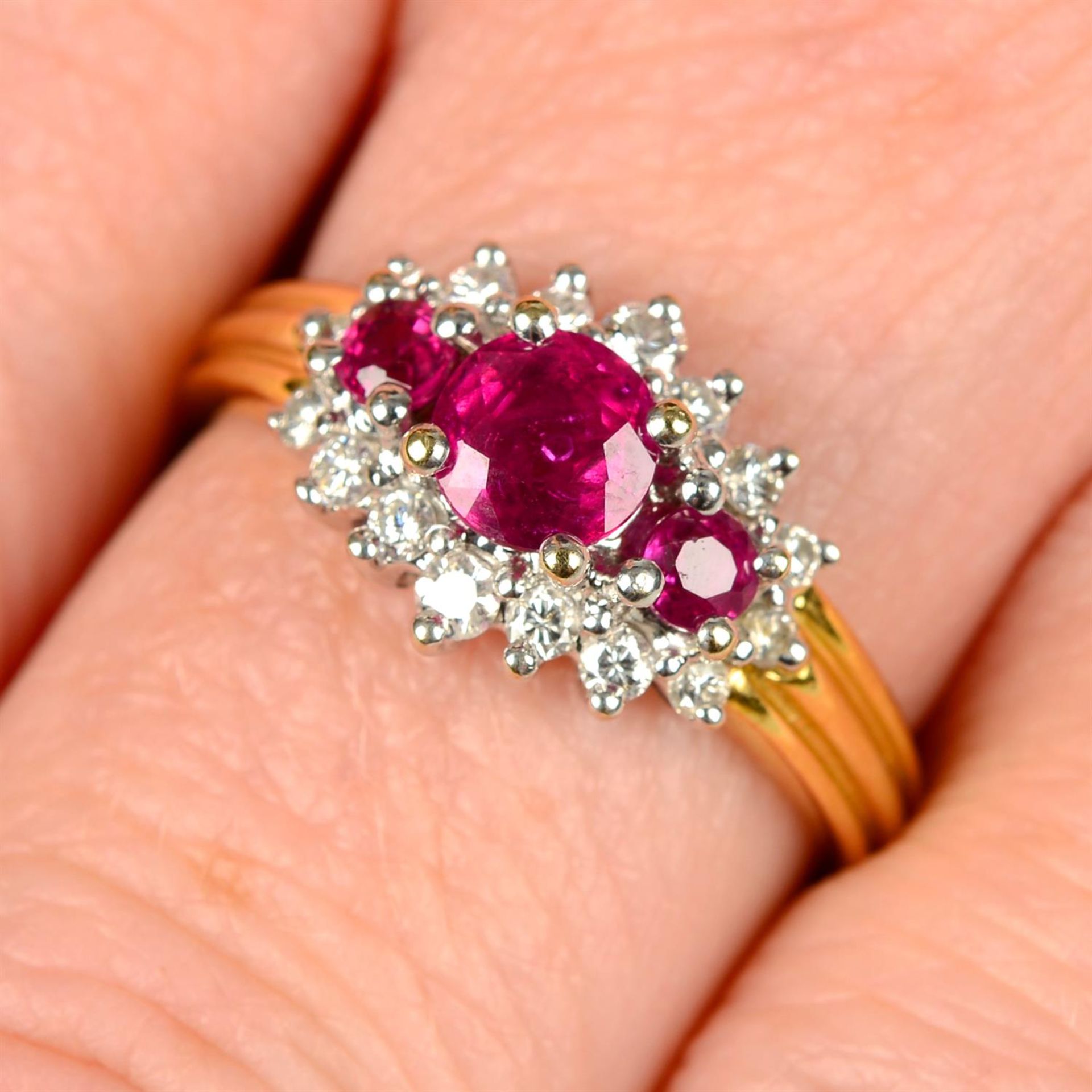 An 18ct gold graduated ruby three-stone ring, with brilliant-cut diamond surround.