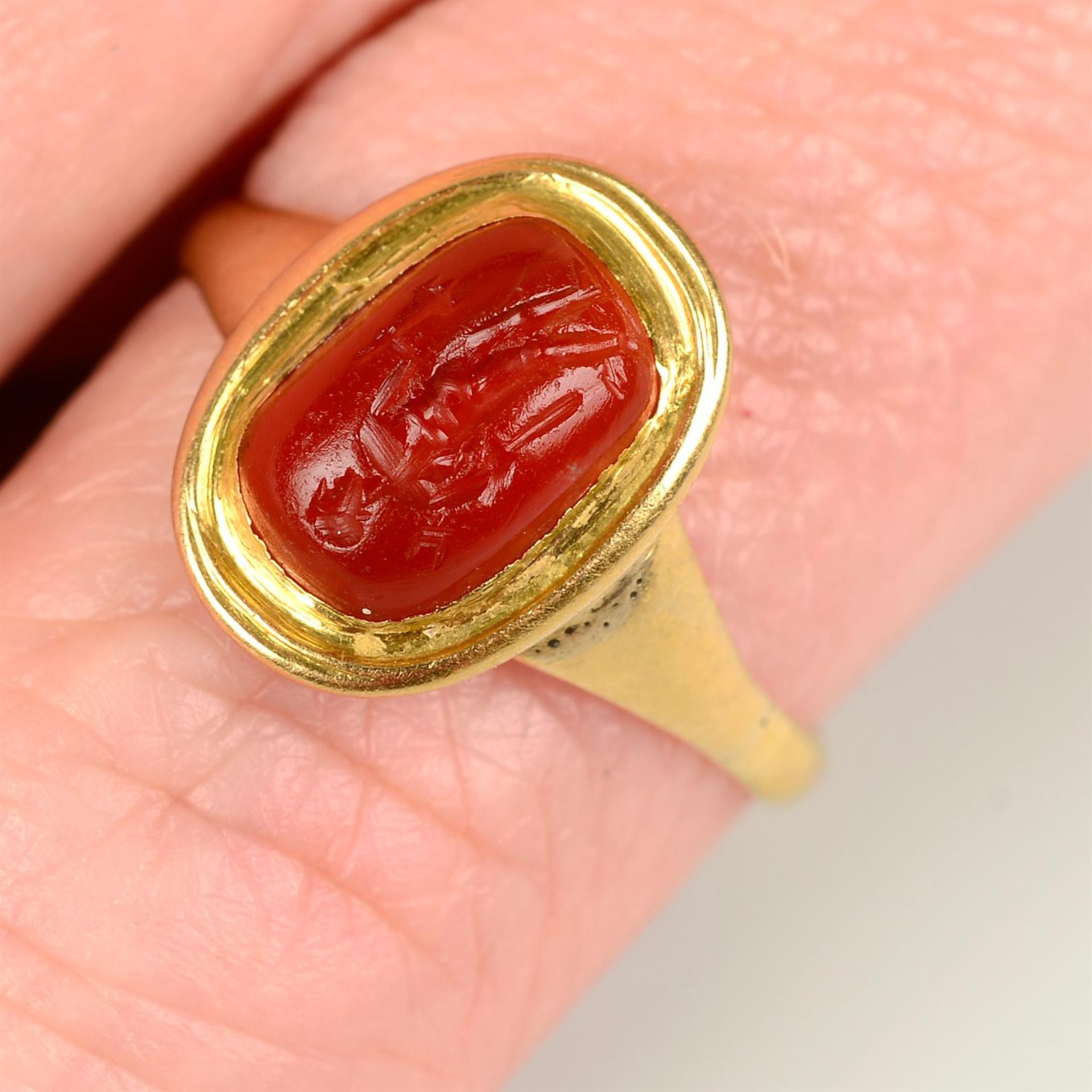An antique carnelian intaglio, carved to depict a man holding a bident and further item,
