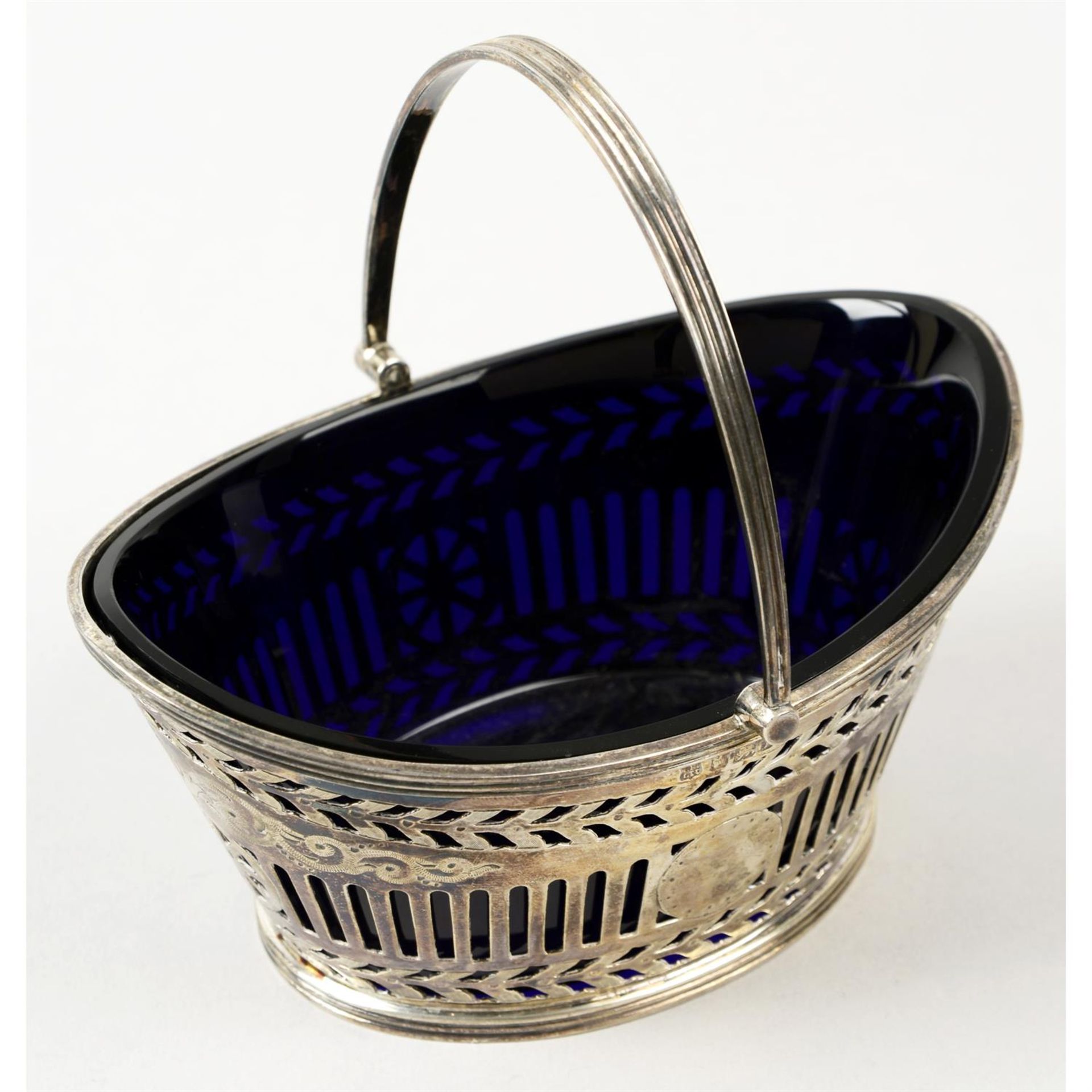 A late Victorian silver pierced swing handle sugar basket, with blue glass liner.