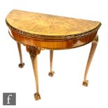 A 1930s walnut fold-over card table of demi lune outline, with acanthus moulded edge and with a