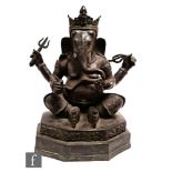 A Tibetan patinated cast metal figure of Ganesh, the Hindu diety, modelled on a throne base, holding