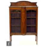 An Edwardian inlaid mahogany display cabinet enclosed by a pair of bar glazed doors below an