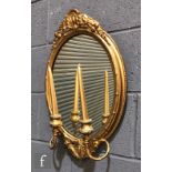 A late 19th Century oval gilt girandole wall mirror, twin scroll branch arms below a pediment,