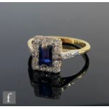 A mid 20th Century 18ct sapphire and diamond cluster ring, central emerald cut sapphire, length 7mm,