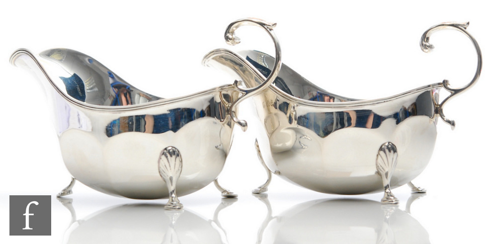 A pair of hallmarked silver sauce boats of plain panelled form terminating in pointed pad feet and