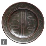 A Winchcombe Pottery dish decorated with brown wavy and straight lines in an oxide glaze against a